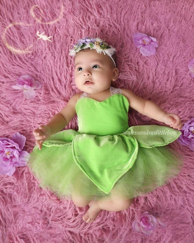 Baby in a green dress lying on a pink textured surface with flowers.
