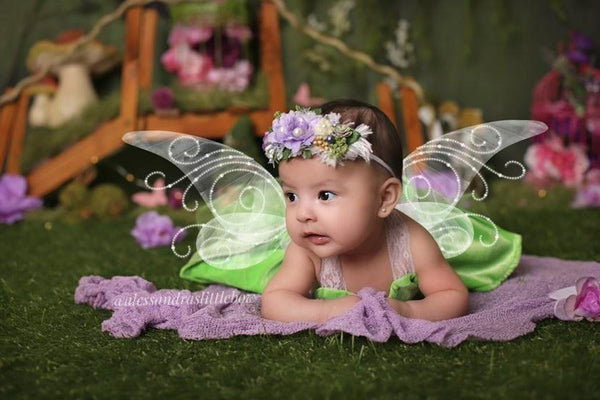 Baby in fairy costume with wings and flower headband on a grassy background