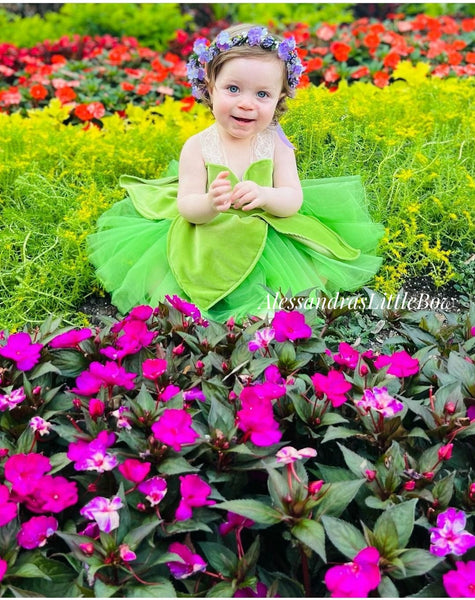 toddler girl in  a green fairy dress with flower crown sitting among flowers